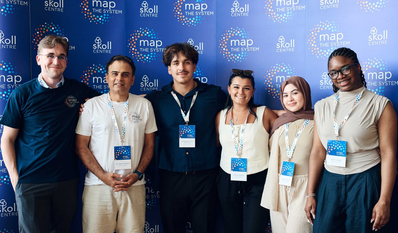 Five university students and a professor stand together in front of a blue backdrop.
