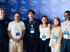 Five university students and a professor stand together in front of a blue backdrop.