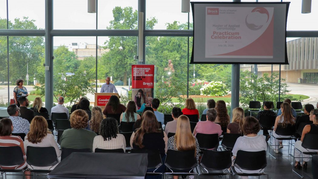 An audience listens to a speaker in a sunny atrium at Brock University.
