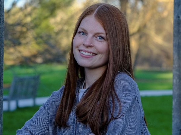 A young woman smiles for a photo with a green space and trees behind her.