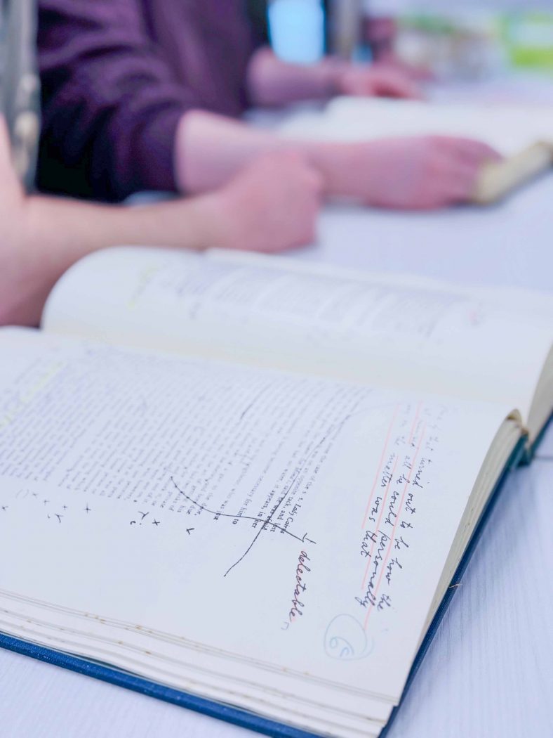 A close up shot of a large, archival tome shows typewriting and handwritten notes on a page.