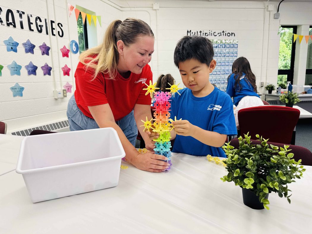 An educator helps a child create a structure using colourful educational toys.