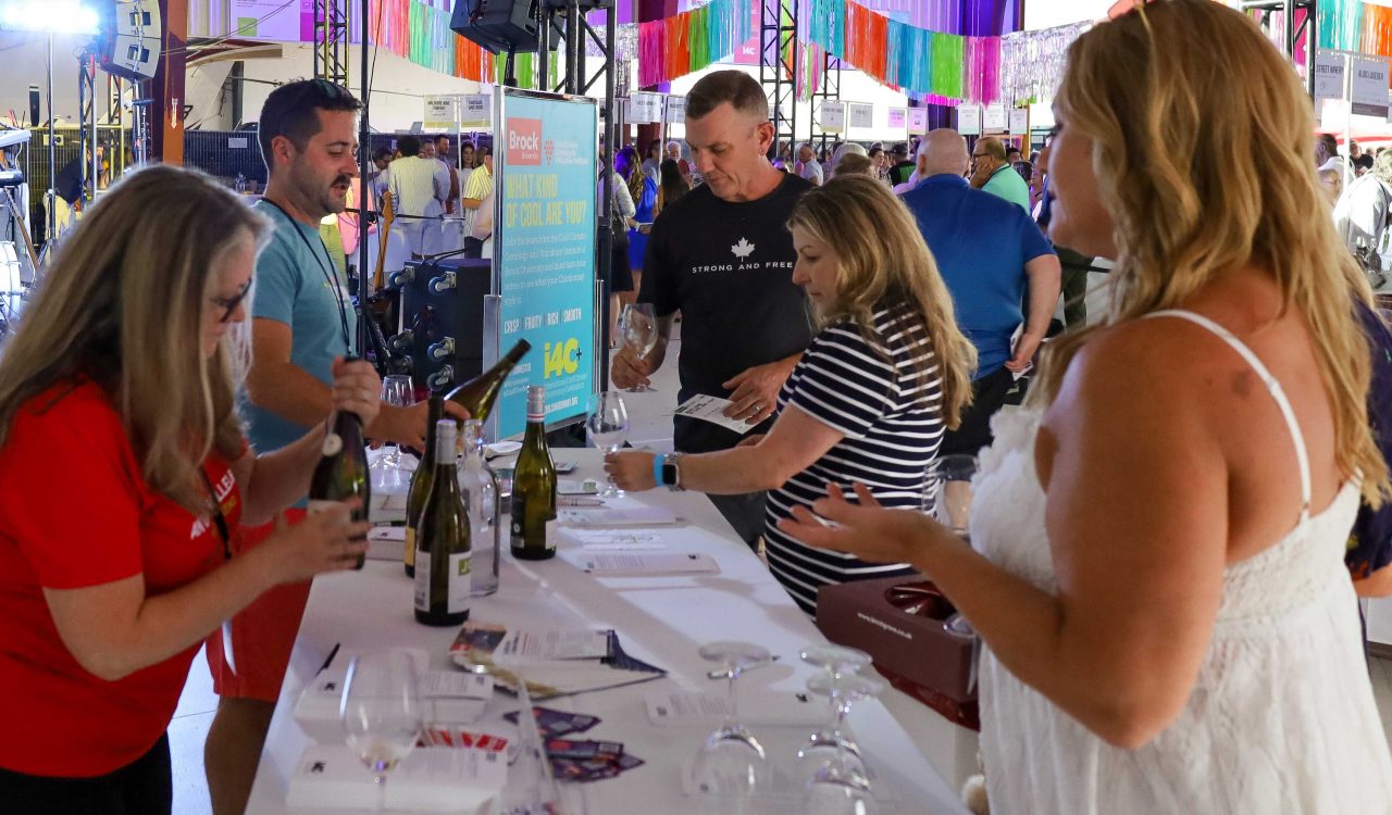 Two CCOVI experts stand behind a table pouring wine for event for International Cool Climate Chardonnay Celebration (i4C) event attendees.