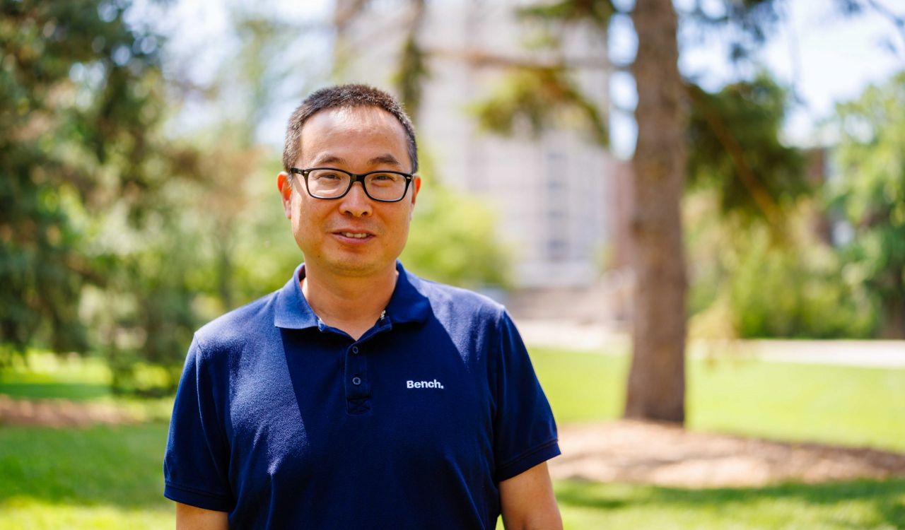 Head-and-shoulders photo of Yifeng Li, with a building, trees and grass blurred out in the background.