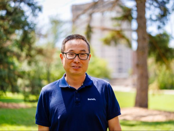 Head-and-shoulders photo of Yifeng Li, with a building, trees and grass blurred out in the background.
