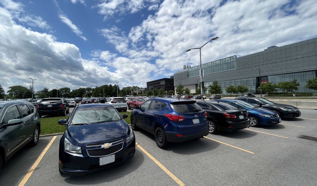 Cars parked in a parking lot on a summer day with a glass building in the background.