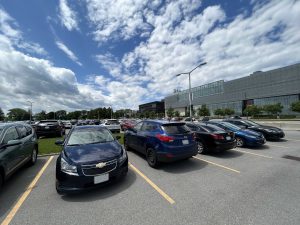 Cars parked in a parking lot on a summer day with a glass building in the background.