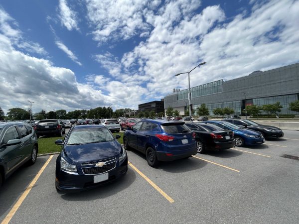 Cars parked in a parking lot on a summer day with a glass building in the background.