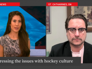 A split screen with two frames, in one a woman in a dress sits at an anchor desk in the Global News studio and in the second frame, a man wearing glasses and a blazer is seated in an office, in front of a couch and paintings on the wall.