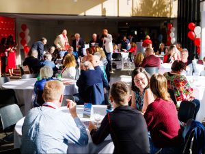 A room full of people sit at table or stand and chat at a university reunion event.