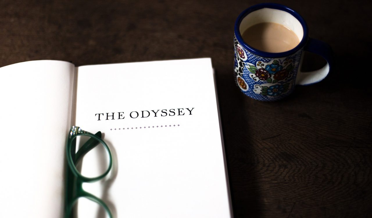 A book opened to the title page, which reads "The Odyssey," beside a cup of tea.
