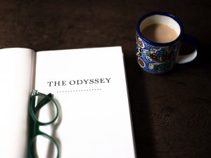 A book opened to the title page, which reads "The Odyssey," beside a cup of tea.