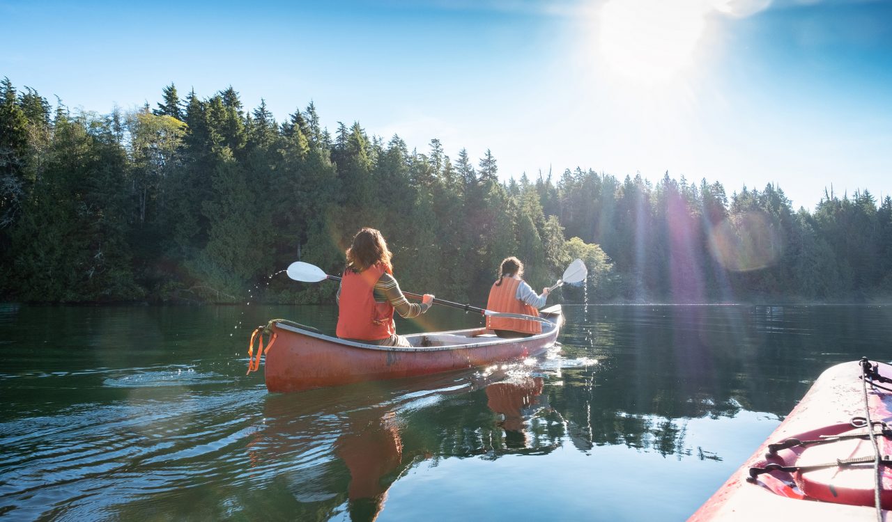 Two women canoe on a scenic lake surrounded by trees.