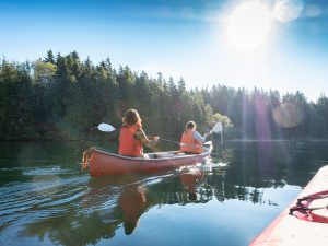 Two women canoe on a scenic lake surrounded by trees.