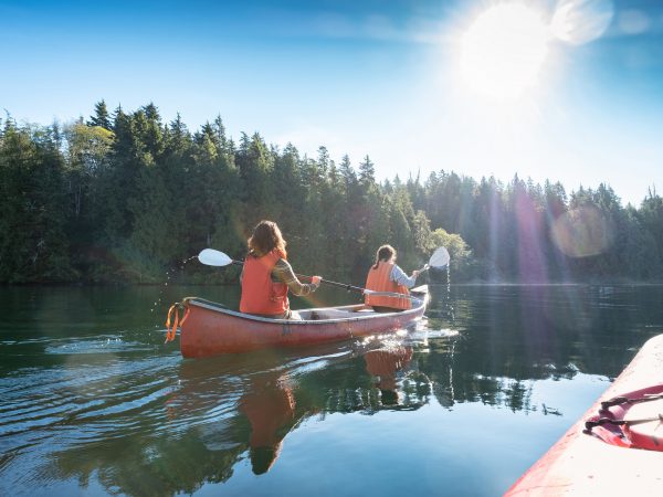 Two women canoe on a scenic lake surrounded by trees.