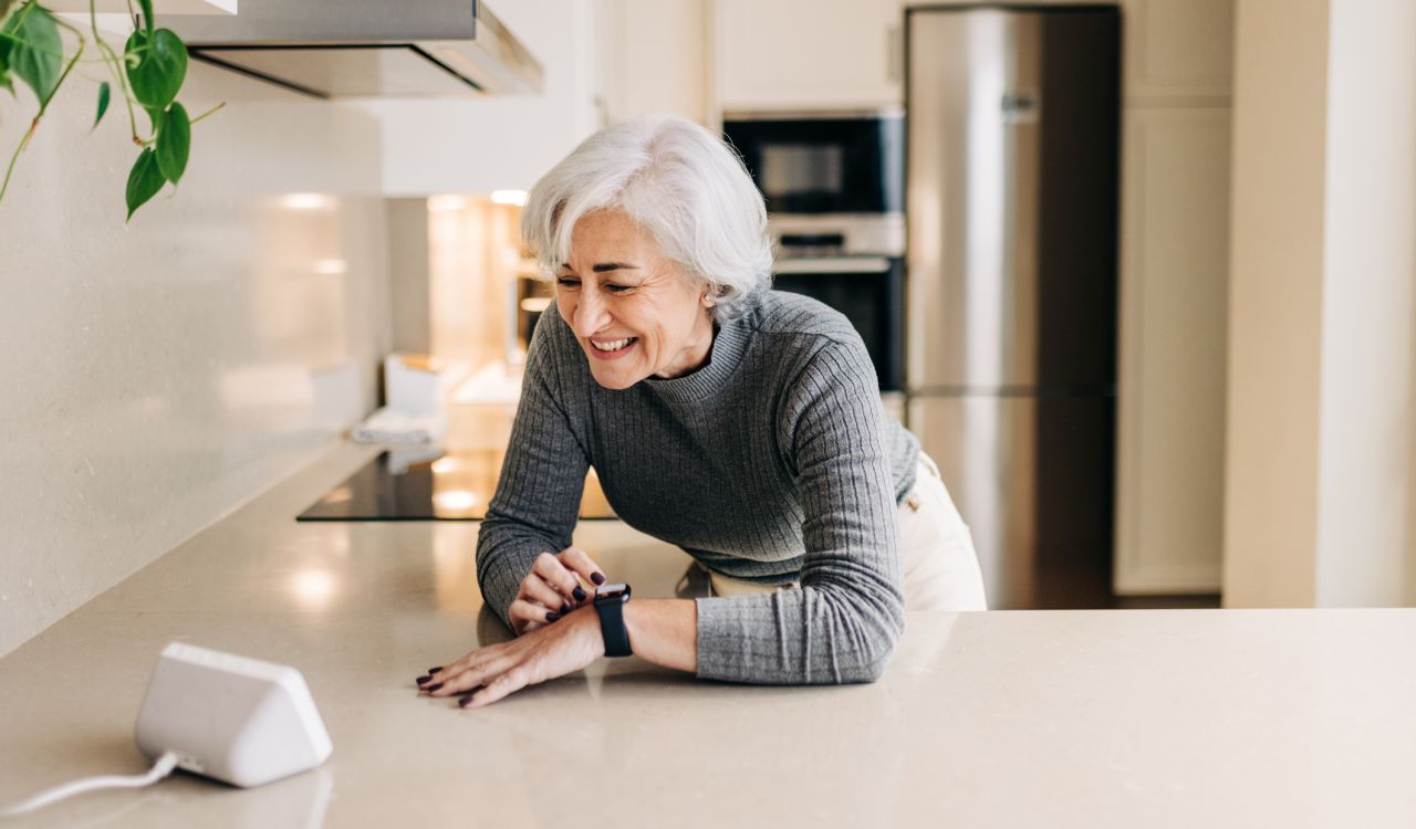 An older woman uses a voice-activated device in her kitchen.