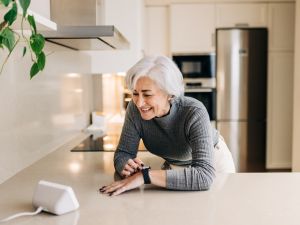 An older woman uses a voice-activated device in her kitchen.