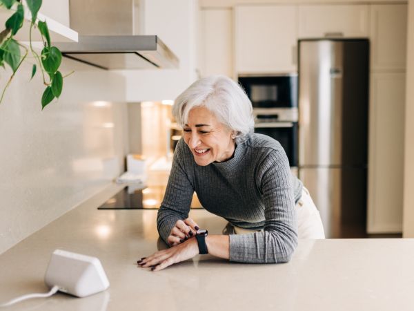 An older woman uses a voice-activated device in her kitchen.