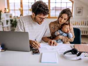 Two young adults look at financial papers while sitting a table with their baby.