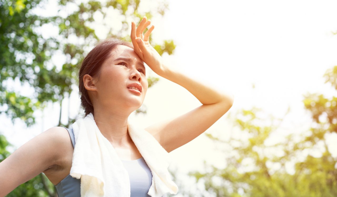 A woman who looks uncomfortable stands outside on a hot day.