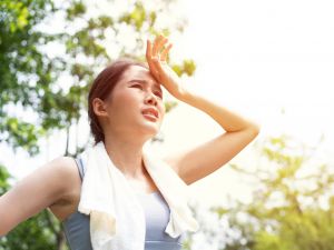 A woman who looks uncomfortable stands outside on a hot day.