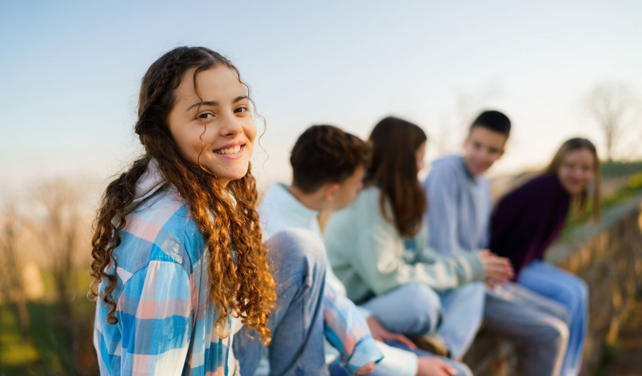 A teenage girl sits outside laughing with friends.