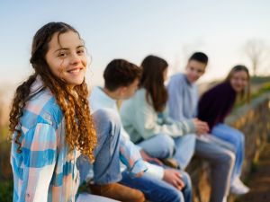A teenage girl sits outside laughing with friends.