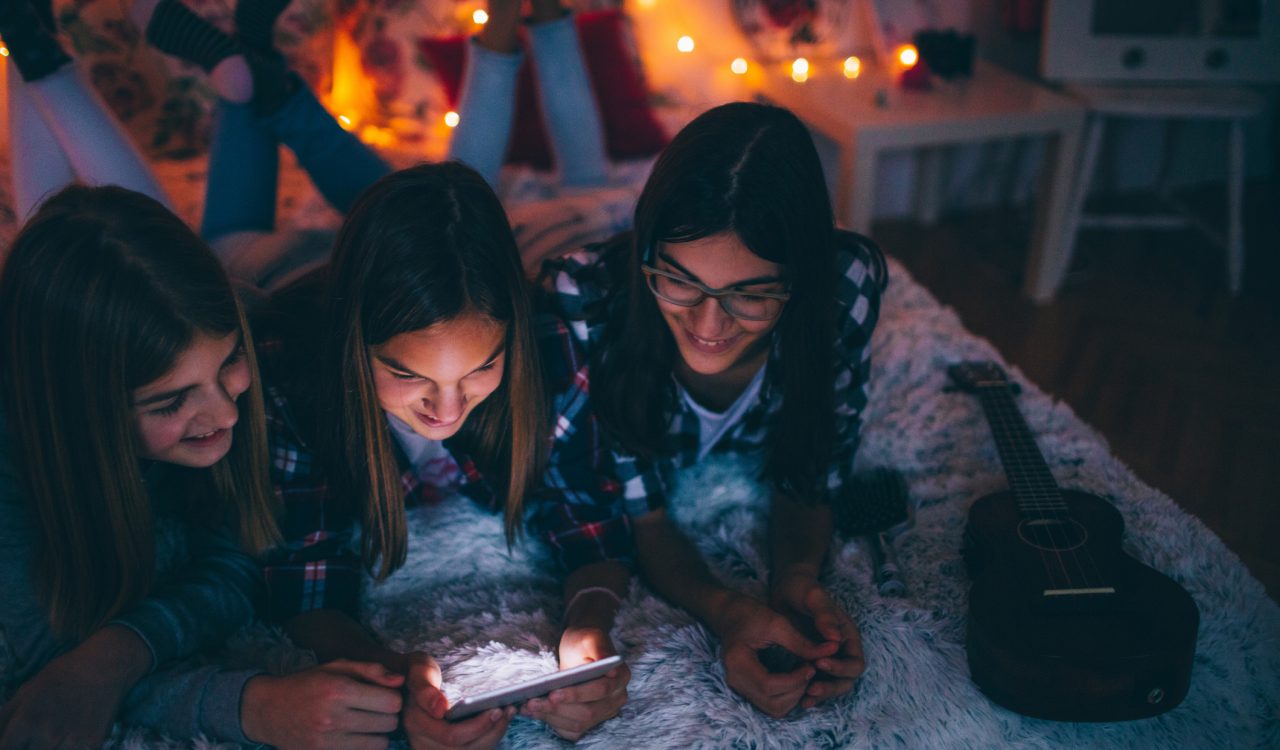 Photo of young teenagers hanging together in a bedroom looking over a smartphone.