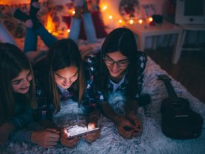 Photo of young teenagers hanging together in a bedroom looking over a smartphone.
