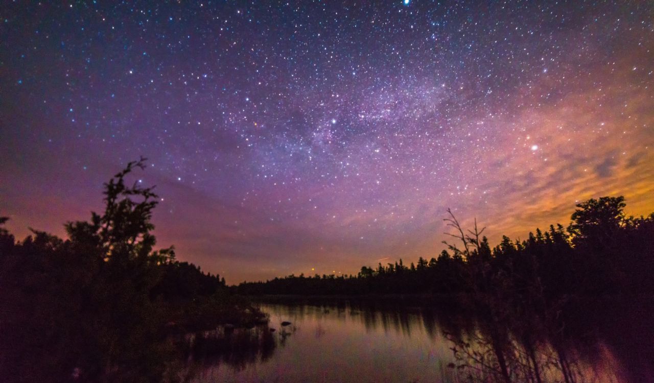 A starry twilight sky above water and a dark shoreline.