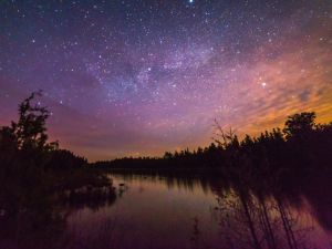 A starry twilight sky above water and a dark shoreline.