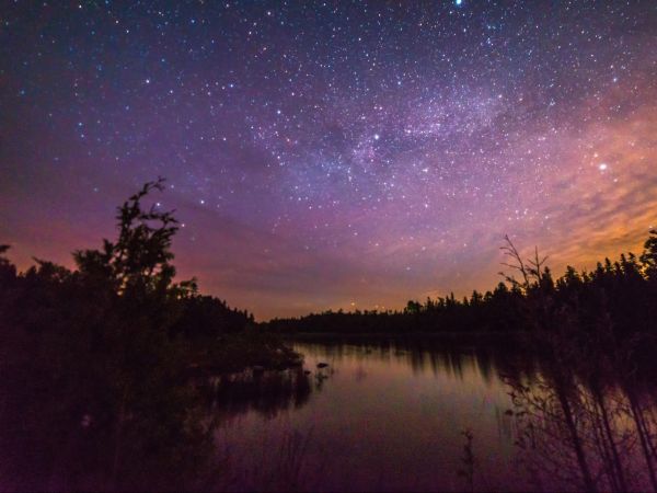 A starry twilight sky above water and a dark shoreline.