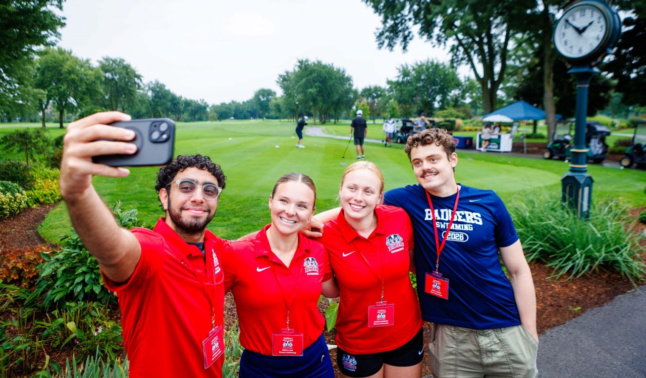 Four university students take a selfie on a golf course.