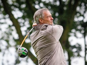 A man swings a golf club in the rain.