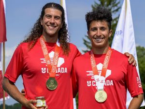 Two men stand against a blue sky wearing red T-shirts and gold medals hanging around their necks.
