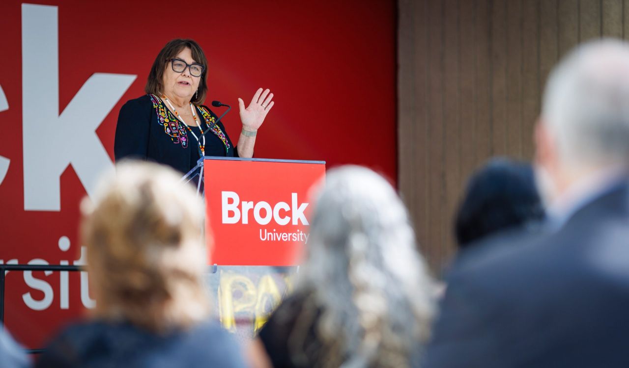 Sheila Cote-Meek speaks at a podium bearing the Brock University logo while addressing an audience at a campus event.
