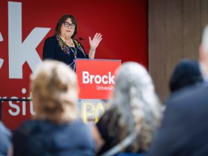 Sheila Cote-Meek speaks at a podium bearing the Brock University logo while addressing an audience at a campus event.