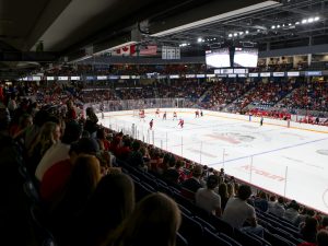 A hockey arena packed with people in the stands and hockey players on the ice.