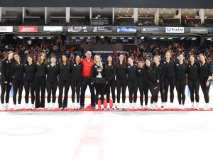 A large group of people stands on the ice of a hockey arena with a trophy in hand.