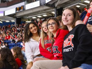 A group of women in Brock University shirts sit in a packed hockey arena.