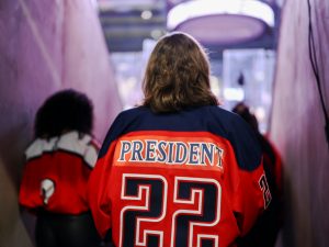 Brock University President and Vice-Chancellor Lesley Rigg walks out onto the ice at a hockey arena. She is shown from behind in a Brock Badgers hockey jersey that says 
