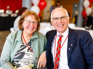 Two people sit next to each other and smile at a university reunion event.