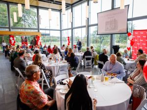 Groups of people sit at at tables during a university reunion event.