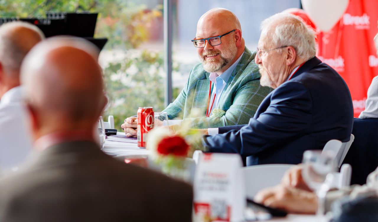 A group of older men sit at a table at a university reunion.