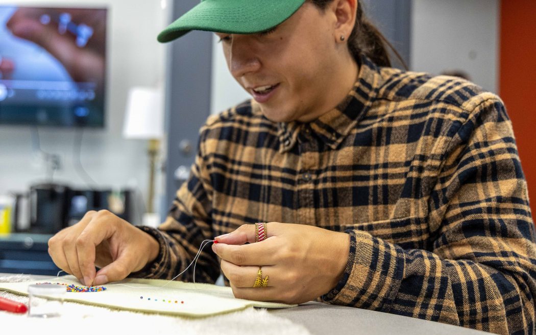 A young man threads beads onto a needle while working on a beading project.