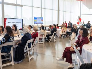 A group of people sit at tables at an event watching on intently as someone not pictured addresses them.