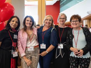 A group of five women smile while standing together.
