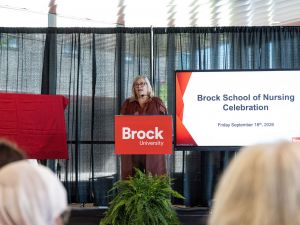 Karyn Taplay, Director and Associate Professor of Brock's School of Nursing speaks into a microphone at a podium while addressing a room of people.