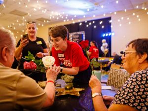 A university student hands a flower to an older person at a volunteering event.