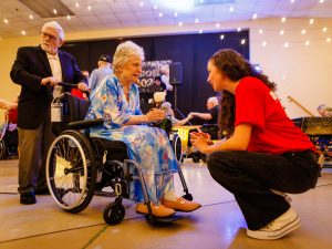 A university student talks to an older woman using a wheelchair at a volunteering event.